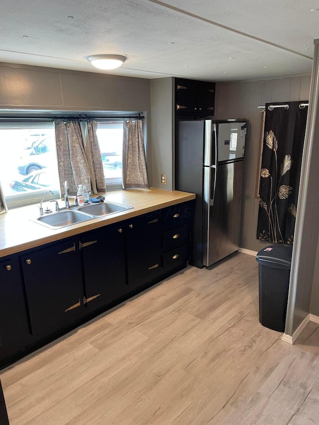 kitchen featuring stainless steel refrigerator, sink, a textured ceiling, and light wood-type flooring