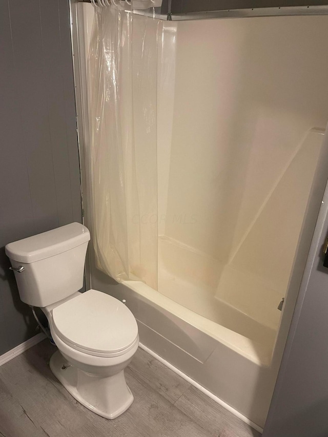 bathroom with hardwood / wood-style floors, shower / bath combination with curtain, and toilet