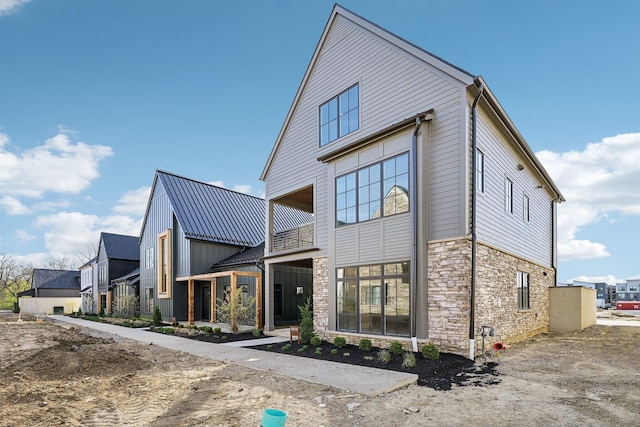 back of house featuring stone siding and a balcony
