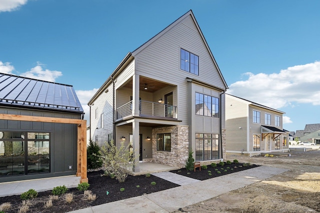 view of front of home featuring a standing seam roof, stone siding, and a balcony