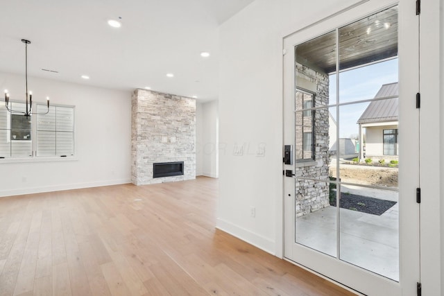unfurnished living room with light wood finished floors, a stone fireplace, baseboards, and an inviting chandelier