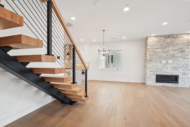 staircase with hardwood / wood-style flooring, a fireplace, baseboards, a notable chandelier, and visible vents