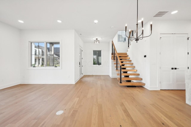 entrance foyer featuring light wood finished floors, baseboards, visible vents, a notable chandelier, and stairway
