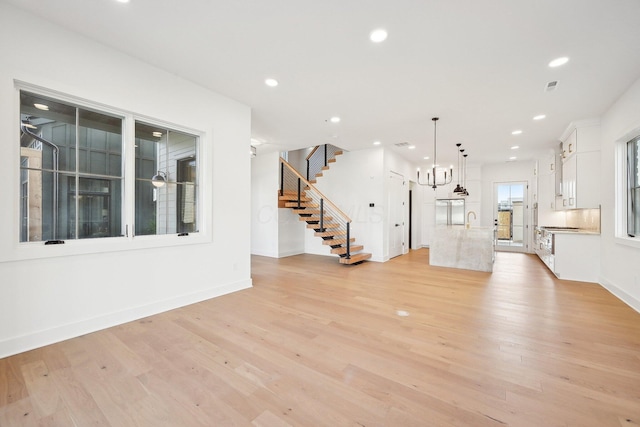 unfurnished living room featuring recessed lighting, light wood-style flooring, and stairway