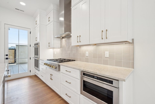kitchen with visible vents, wall chimney exhaust hood, tasteful backsplash, appliances with stainless steel finishes, and white cabinetry