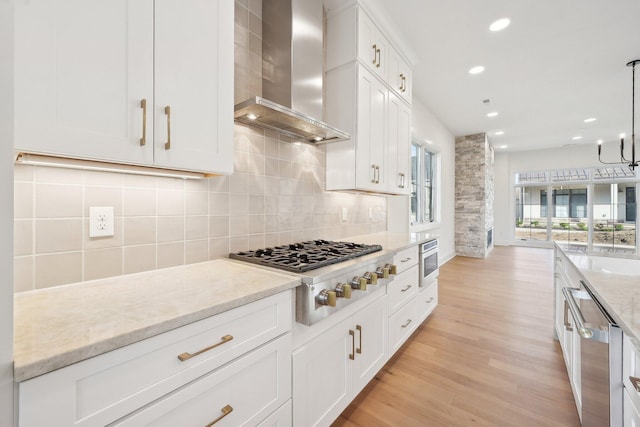 kitchen featuring white cabinets, stainless steel appliances, recessed lighting, decorative backsplash, and wall chimney range hood