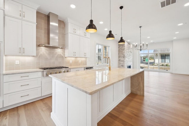 kitchen with wall chimney exhaust hood, a sink, light wood-type flooring, visible vents, and stainless steel gas stovetop