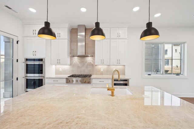 kitchen featuring wall chimney range hood, light stone counters, decorative backsplash, appliances with stainless steel finishes, and visible vents
