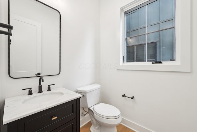 half bathroom with wood finished floors, vanity, toilet, and baseboards