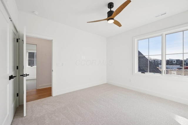 carpeted spare room with baseboards, a ceiling fan, and visible vents