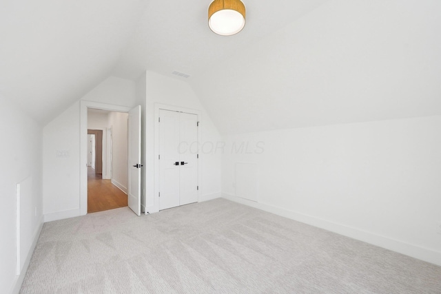 additional living space with baseboards, vaulted ceiling, visible vents, and light colored carpet