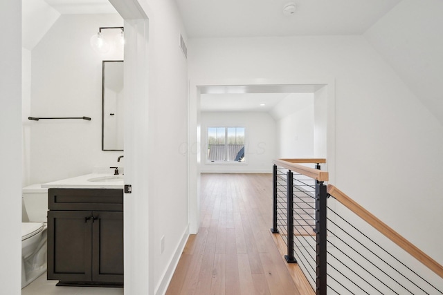 corridor featuring a sink, light wood-type flooring, baseboards, visible vents, and an upstairs landing