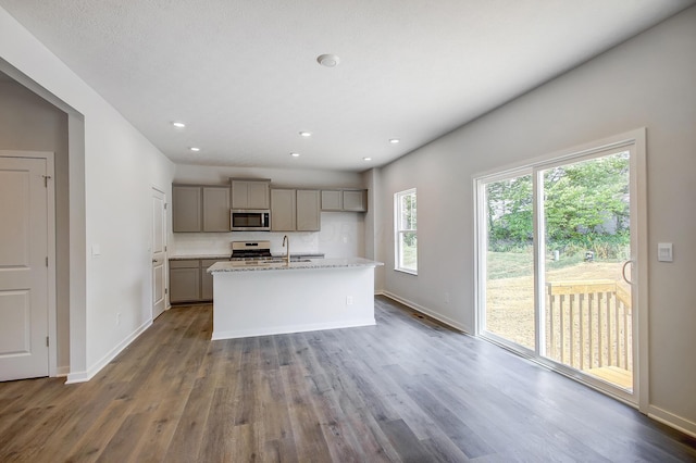 kitchen featuring gray cabinets, an island with sink, appliances with stainless steel finishes, light stone counters, and wood-type flooring