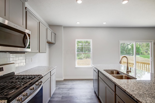 kitchen with sink, dark wood-type flooring, stainless steel appliances, tasteful backsplash, and light stone counters