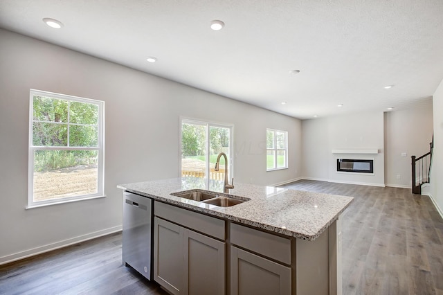 kitchen with gray cabinetry, sink, dark wood-type flooring, stainless steel dishwasher, and a center island with sink