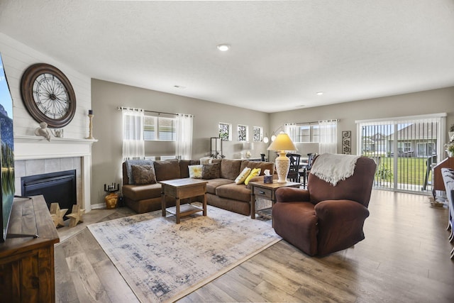 living room with a tile fireplace, a textured ceiling, and light hardwood / wood-style flooring