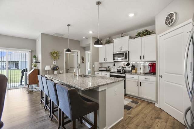 kitchen featuring appliances with stainless steel finishes, light stone counters, sink, decorative light fixtures, and an island with sink