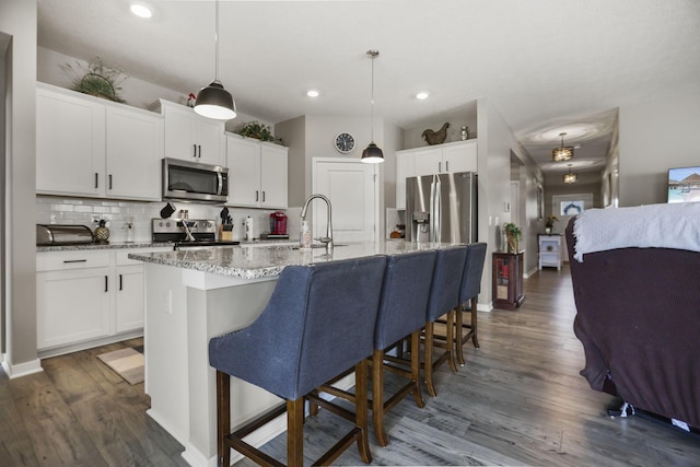 kitchen with dark hardwood / wood-style floors, decorative light fixtures, a kitchen island with sink, white cabinets, and appliances with stainless steel finishes