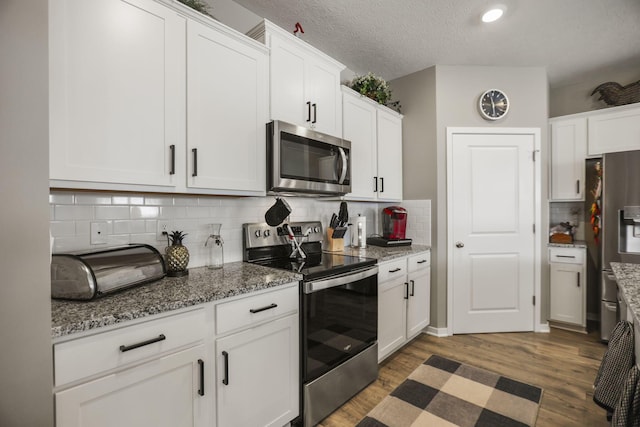 kitchen with dark wood-type flooring, a textured ceiling, appliances with stainless steel finishes, tasteful backsplash, and white cabinetry