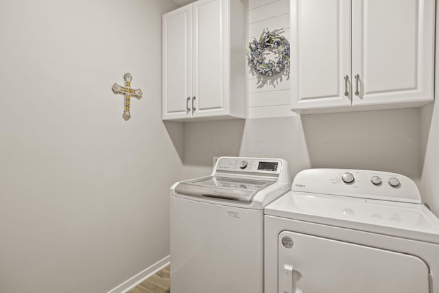 clothes washing area featuring washing machine and clothes dryer, hardwood / wood-style floors, and cabinets