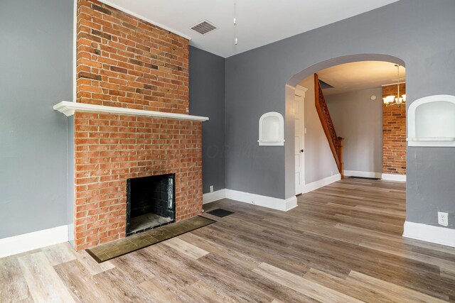 unfurnished living room featuring hardwood / wood-style floors, a brick fireplace, and a notable chandelier