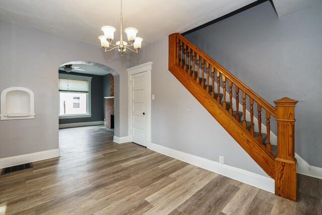 stairway featuring ceiling fan with notable chandelier, wood-type flooring, and a fireplace