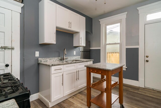 kitchen featuring hardwood / wood-style floors, black range, white cabinetry, and sink