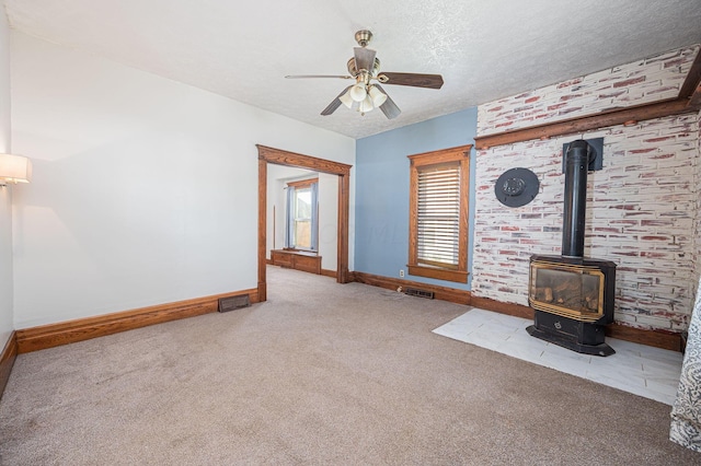 unfurnished living room featuring ceiling fan, light colored carpet, a wood stove, and a textured ceiling