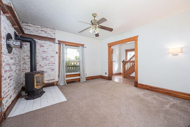 unfurnished living room featuring ceiling fan, light colored carpet, a wood stove, and brick wall