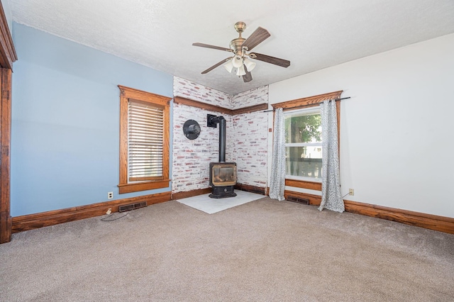 unfurnished living room featuring carpet, a textured ceiling, a wood stove, and ceiling fan