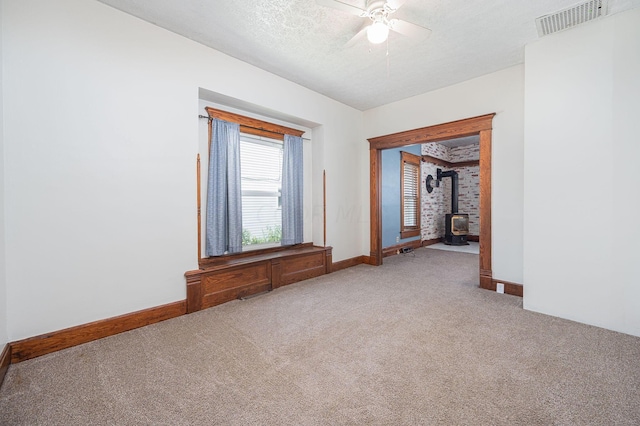 carpeted empty room with a textured ceiling, a wood stove, and ceiling fan