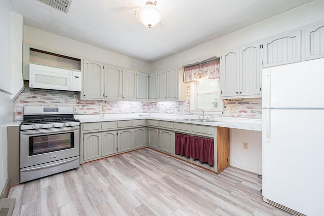 kitchen with white appliances, light hardwood / wood-style floors, tasteful backsplash, and sink