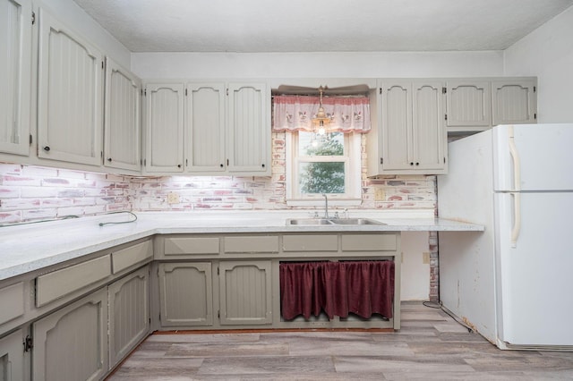 kitchen with sink, hanging light fixtures, tasteful backsplash, light hardwood / wood-style flooring, and white fridge