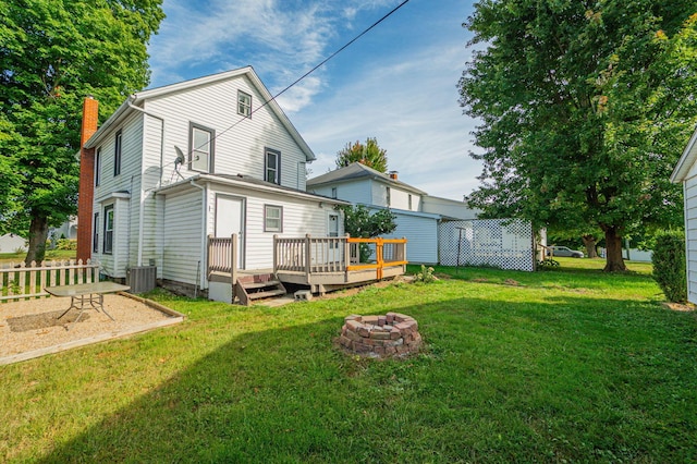 back of house with central air condition unit, a fire pit, a lawn, and a wooden deck