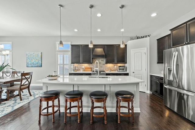 kitchen featuring stainless steel fridge with ice dispenser, a center island with sink, custom range hood, and pendant lighting