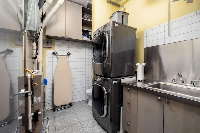 laundry area featuring sink, stacked washing maching and dryer, tile walls, and water heater