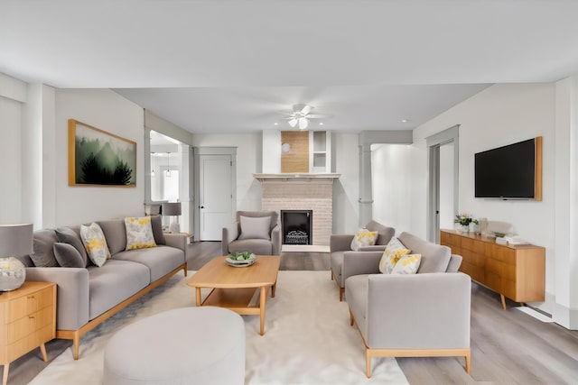 living room with ceiling fan, light wood-type flooring, and a brick fireplace