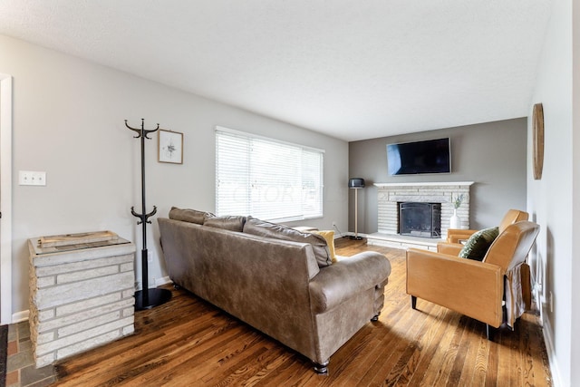 living room with a stone fireplace and dark hardwood / wood-style flooring