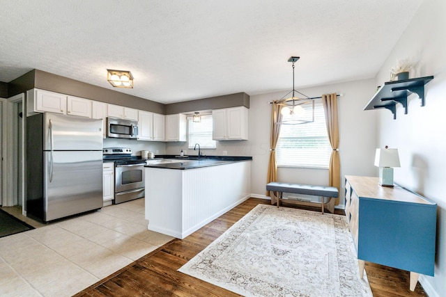 kitchen with stainless steel appliances, sink, decorative light fixtures, light hardwood / wood-style floors, and white cabinetry