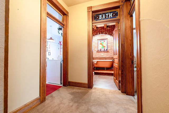 hall with washer / dryer, light carpet, and brick wall