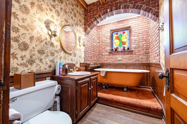 bathroom with brick wall, a washtub, vanity, hardwood / wood-style flooring, and toilet