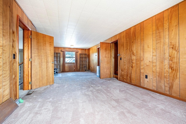 empty room featuring wood walls and light colored carpet