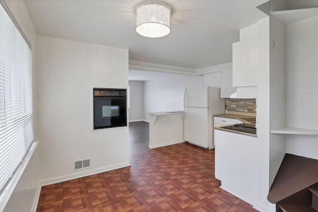 kitchen featuring dark parquet floors, white refrigerator, tasteful backsplash, black oven, and white cabinetry