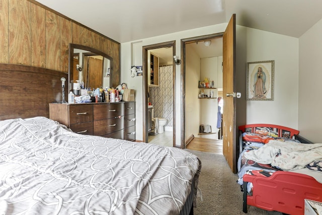 bedroom with vaulted ceiling, light colored carpet, ensuite bath, and wood walls