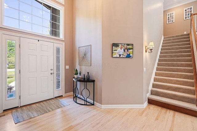 foyer entrance featuring a towering ceiling, light hardwood / wood-style floors, and ornamental molding