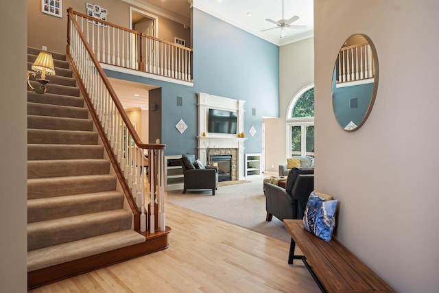 interior space featuring ornamental molding, ceiling fan, hardwood / wood-style flooring, a fireplace, and a high ceiling