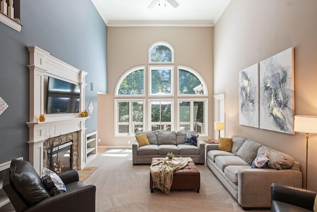 carpeted living room with a high ceiling, a stone fireplace, ceiling fan, and ornamental molding