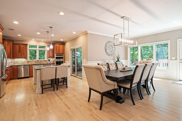 dining space with a chandelier, crown molding, a healthy amount of sunlight, and light wood-type flooring