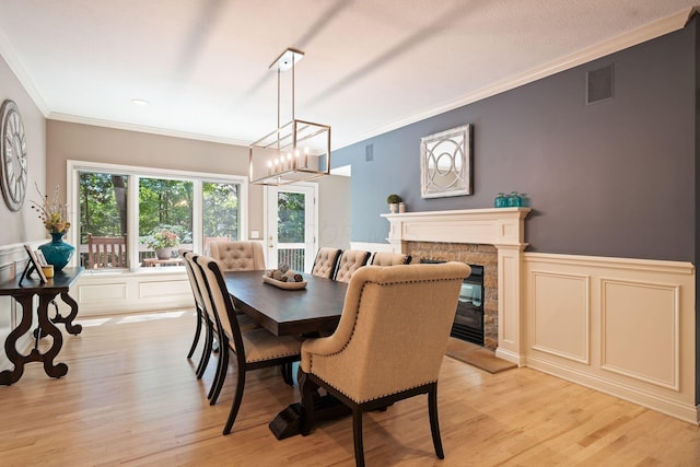 dining area with a stone fireplace, crown molding, light hardwood / wood-style flooring, and a chandelier