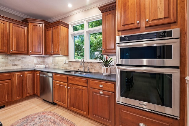 kitchen with tasteful backsplash, ornamental molding, stainless steel appliances, sink, and light hardwood / wood-style flooring